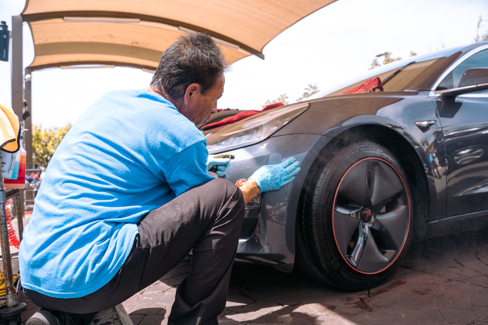 A crew member polishing the wheel and fender of a dark Tesla