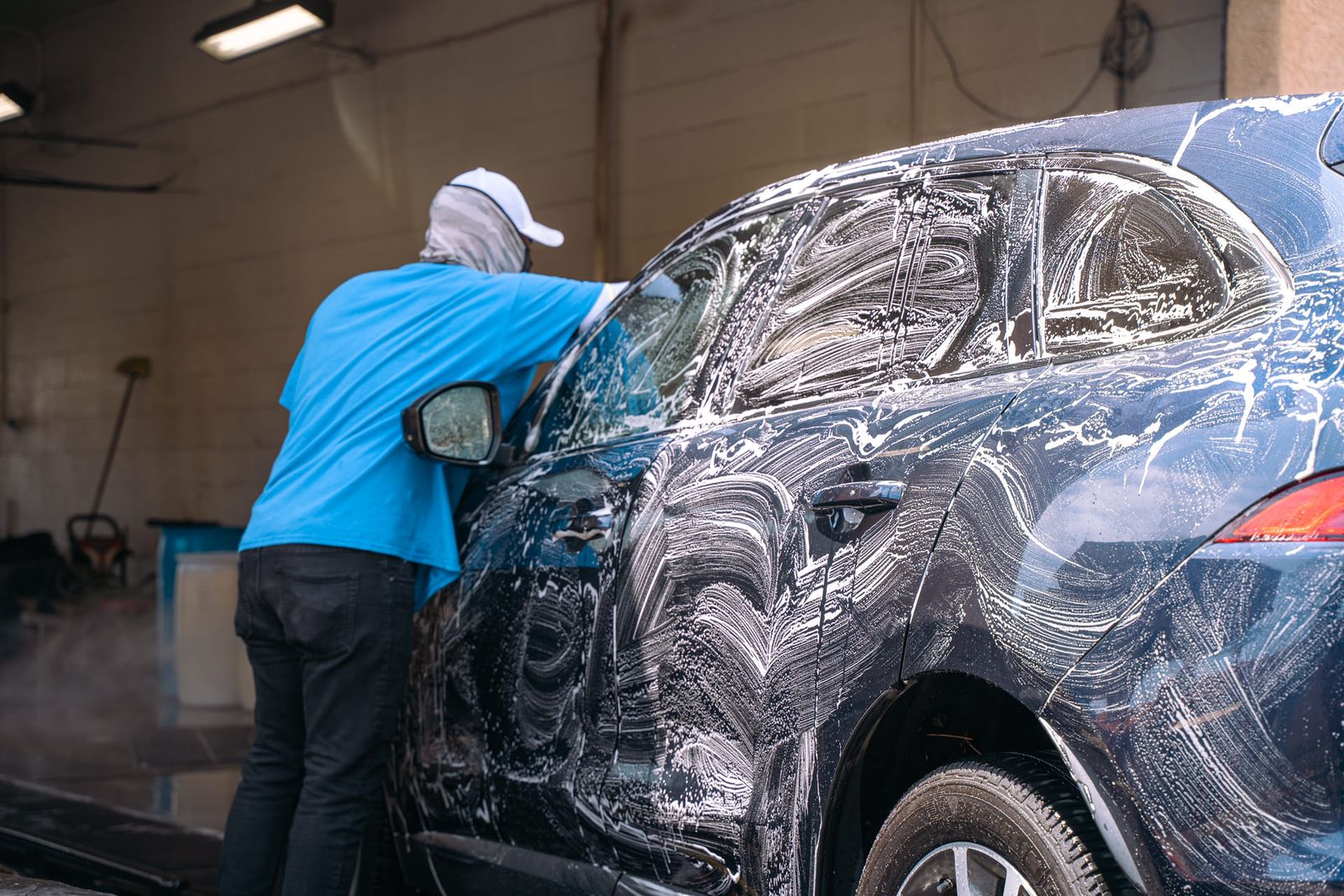 A crew member hand-washing a soaped-up black SUV in the wash bay