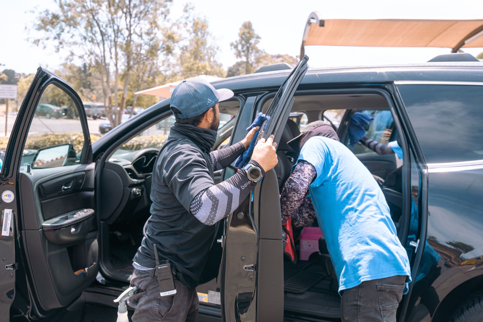 Crew members cleaning the interior of an SUV through its open doors